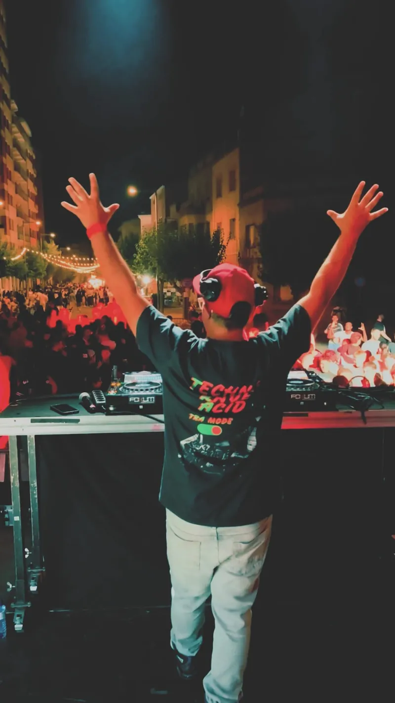 DJ Feren con los brazos en alto animando a la pista en una fiesta al aire libre